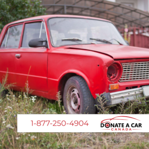 Antique cherry red scrap car missing its headlight text with phone number for Donate a Car