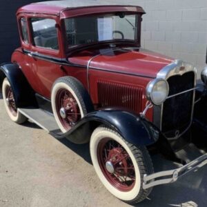 Donated burgundy 1931 FORD MODEL A with red hubs and white wall tires parked in front of a gray wall awaiting auction sale so that donation can be sent to the donor's charity of choice.