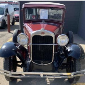 Front view of donated burgundy 1931 FORD MODEL A with red hubs and white wall tires parked in front of a gray wall awaiting auction sale so that donation can be sent to the donor's charity of choice.