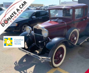 Burgundy 1931 Ford Model A 2D Coupe with whitewall tires parked in front of vehicle auction house. Donate a Car Canada and Canadian Cancer Society logos are posted near the front of the car because the car has been donated for the CCS.